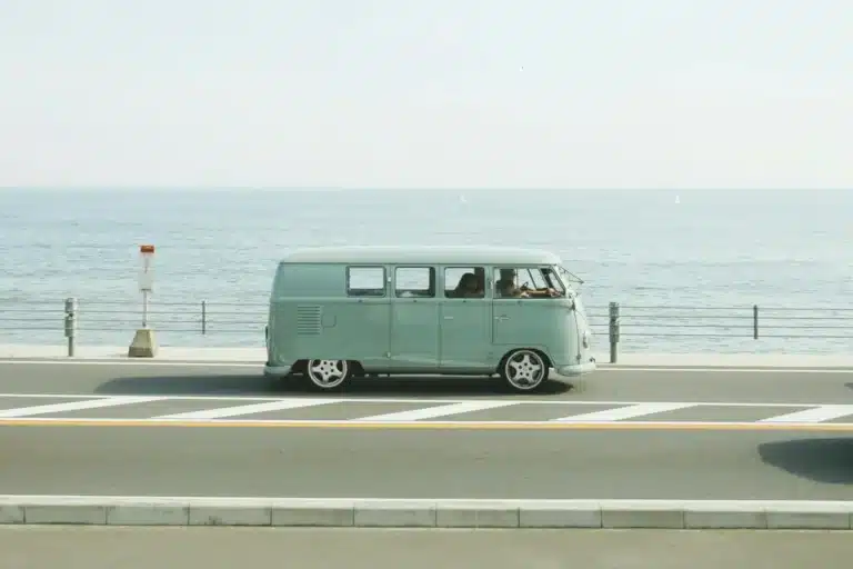Volkswagen T1 de color verde en una carretera con el mar al fondo
